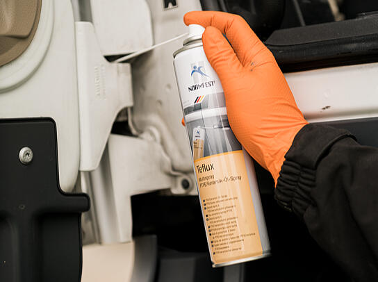 ... Le multispray TEFLUX de Normfest est pulvérisé sur une charnière de porte d'une voiture.